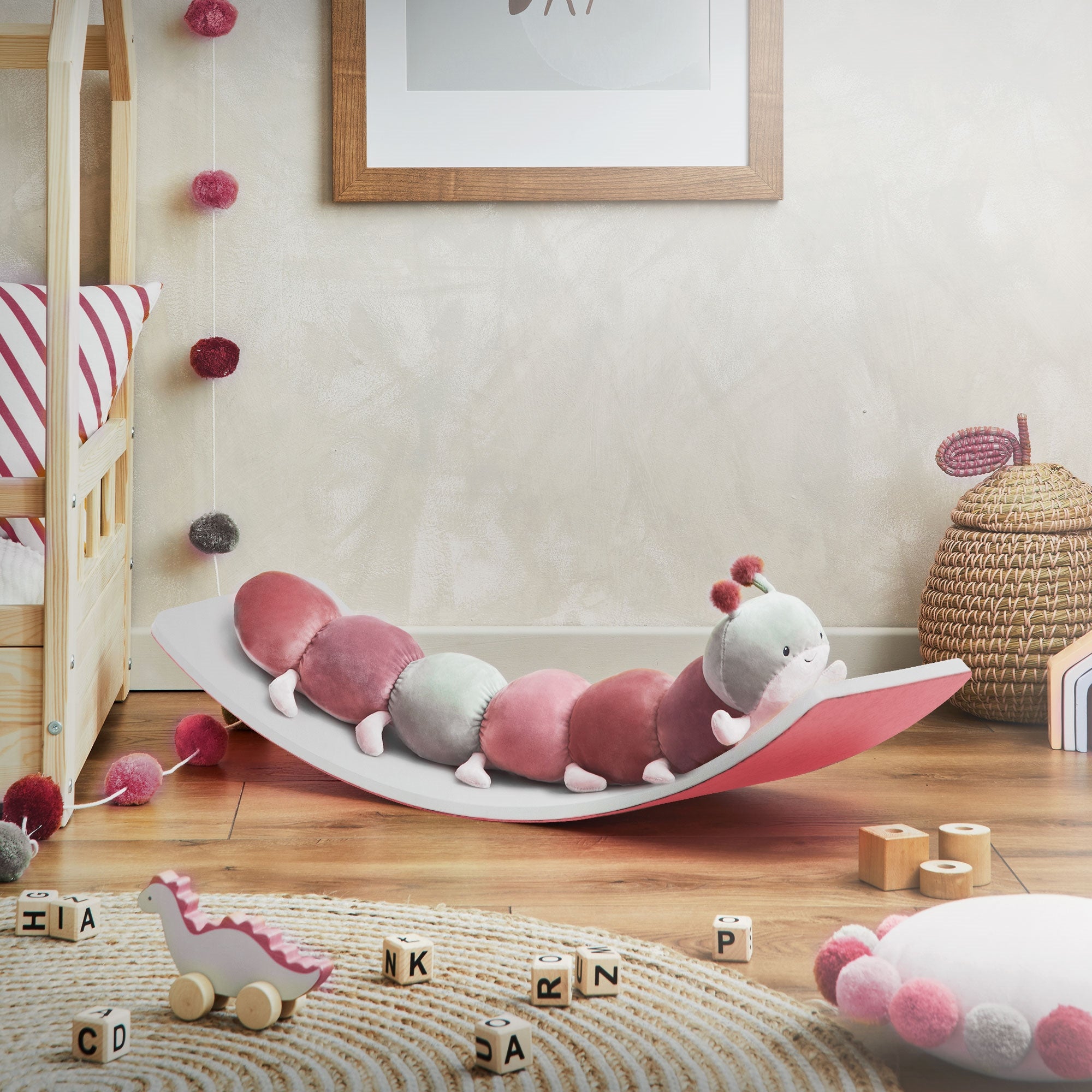 A wobble board with a pink and green caterpillar toy. Toy and decoration in the background.