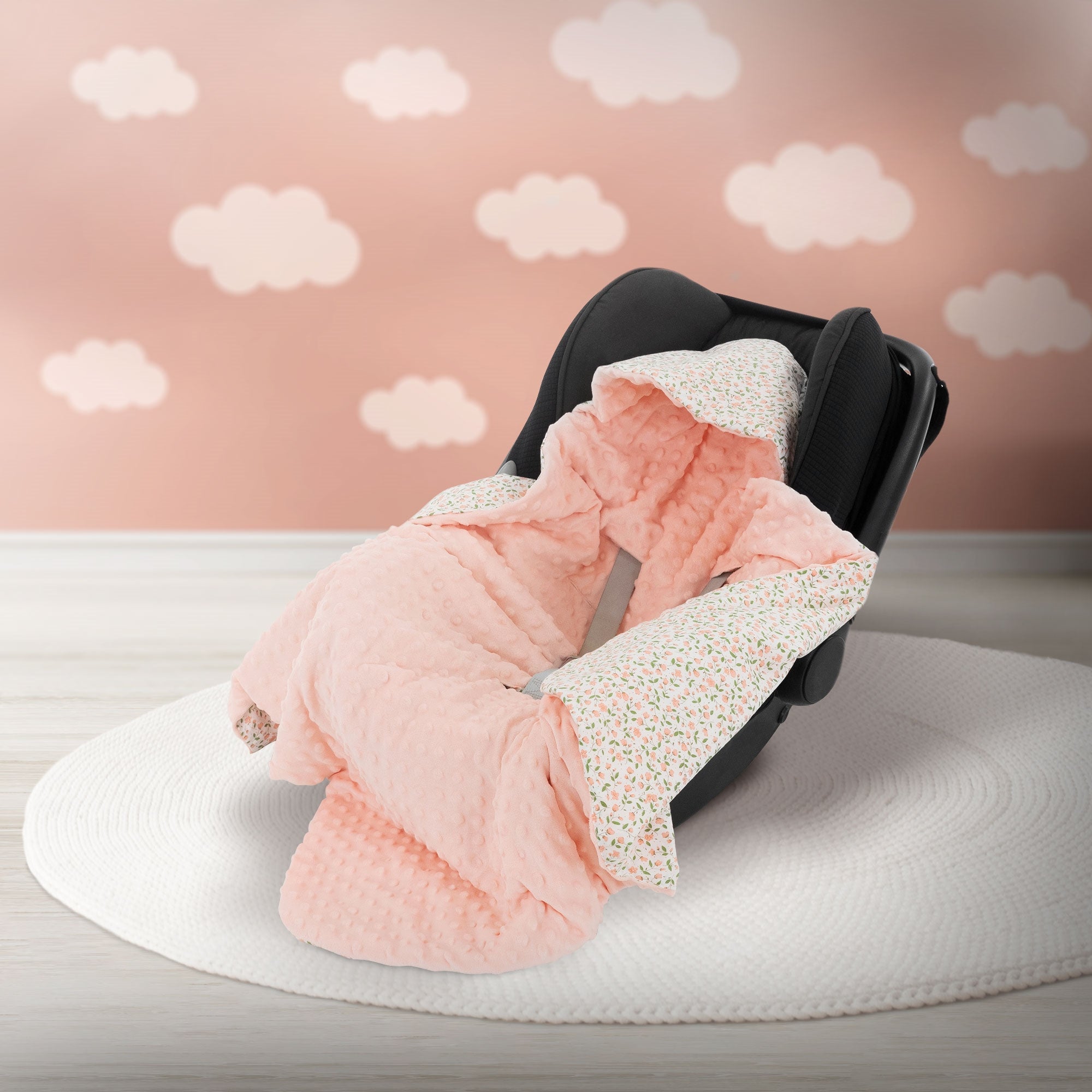 Un asiento de auto negro con una manta rosa sobre una alfombra redonda frente a una pared rosa con nubes.