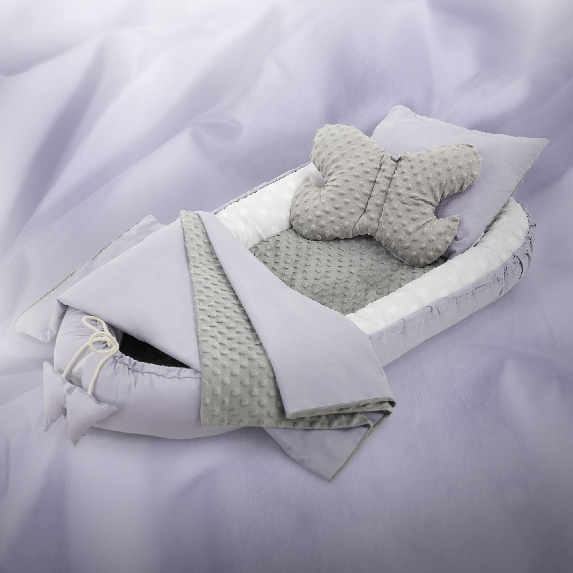 Ein graues Babybett mit einem Schmetterlingskissen und einer Decke.