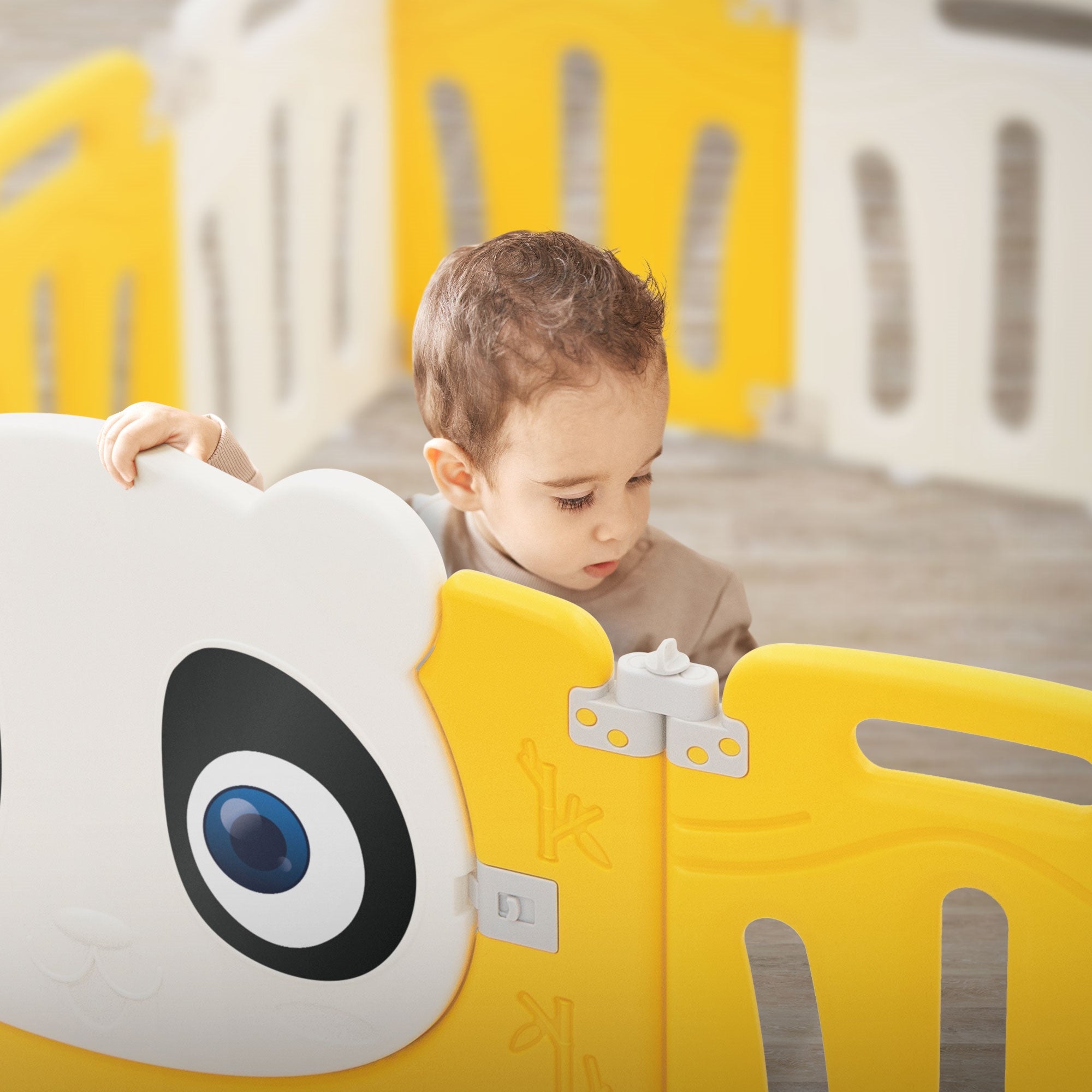 Un enfant se tient devant une clôture de jeu jaune avec un visage de panda.