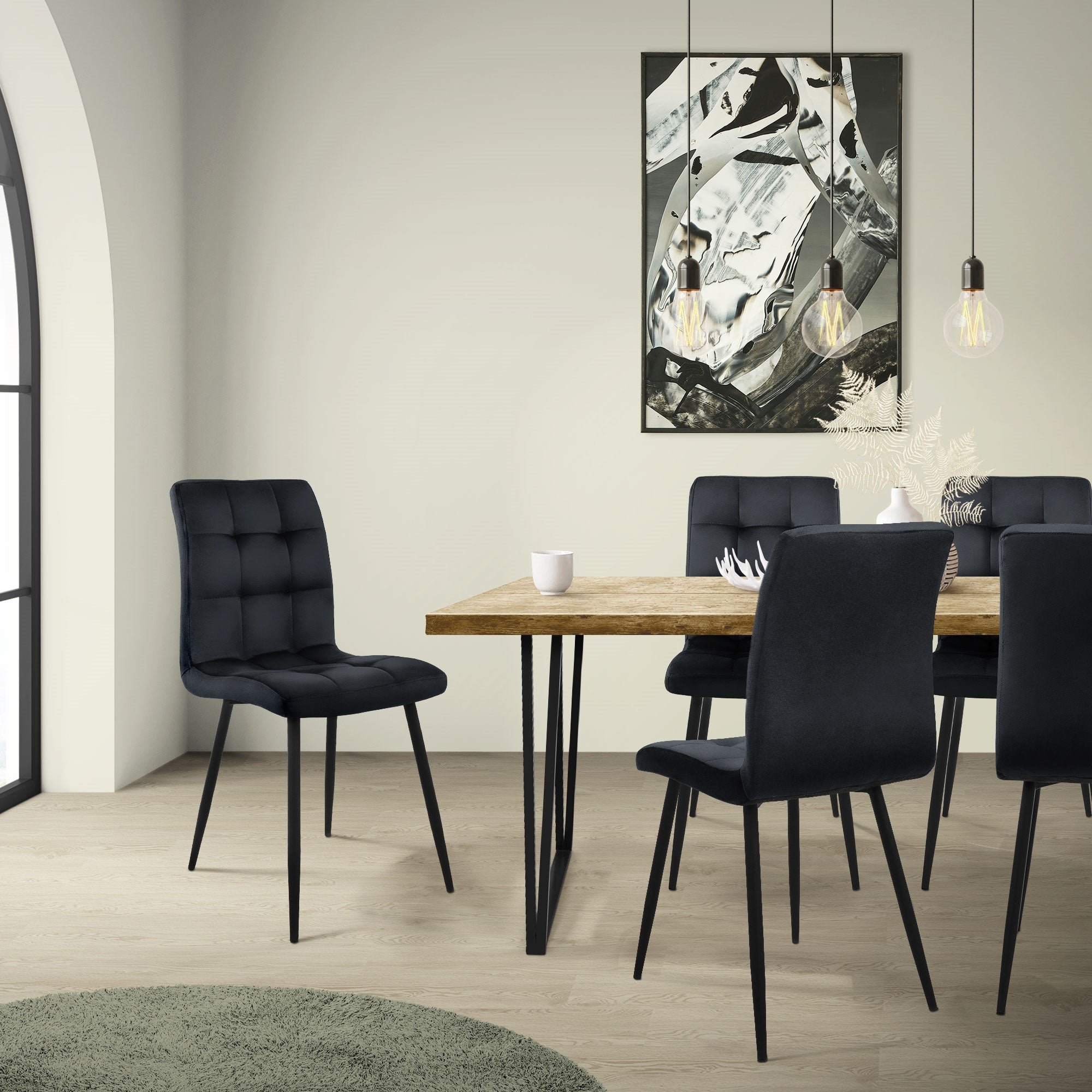 Salle à manger avec une table en bois et des chaises noires, éclairée par des lampes suspendues.