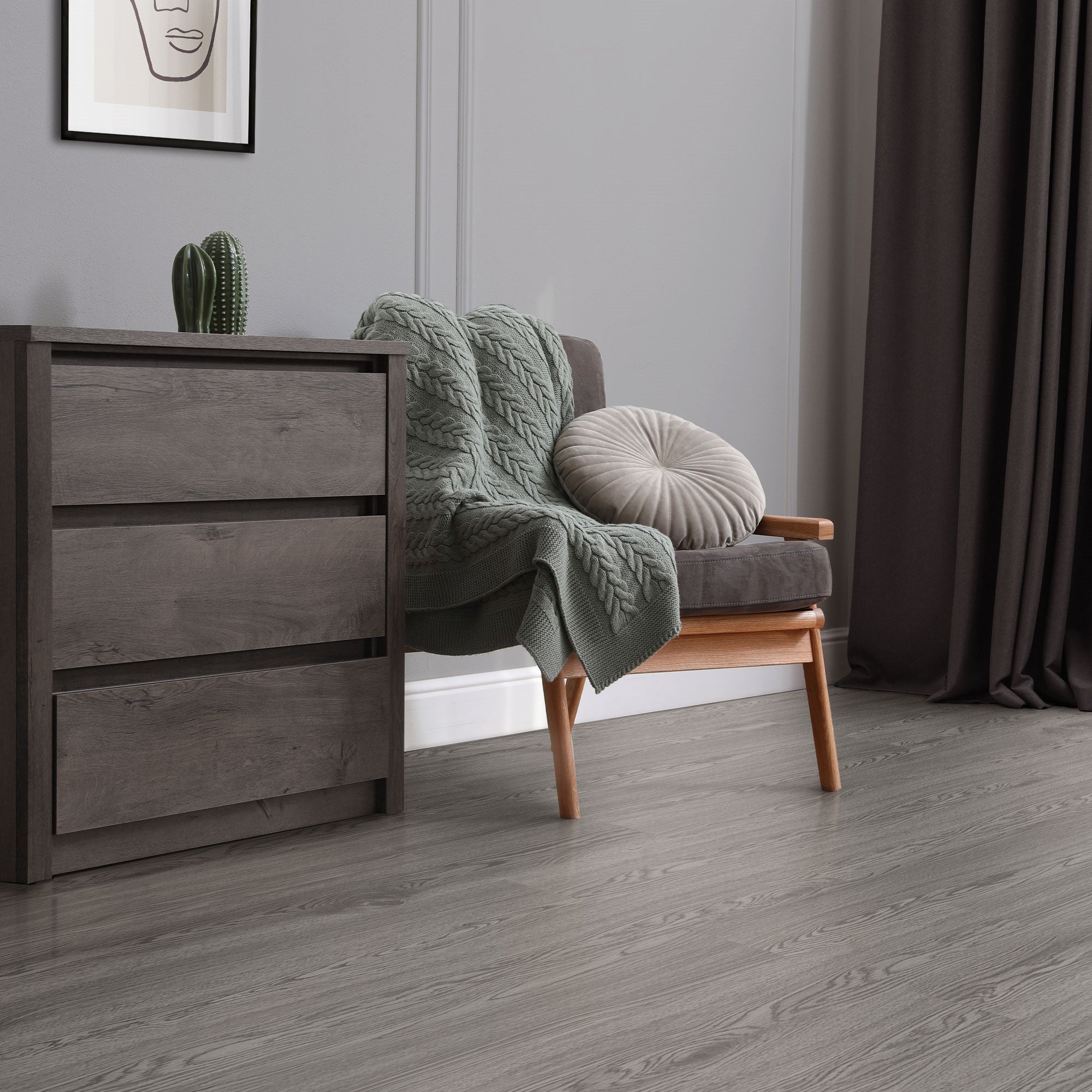 Woonkamer met grijze vloer, fauteuil, kussens en plant.