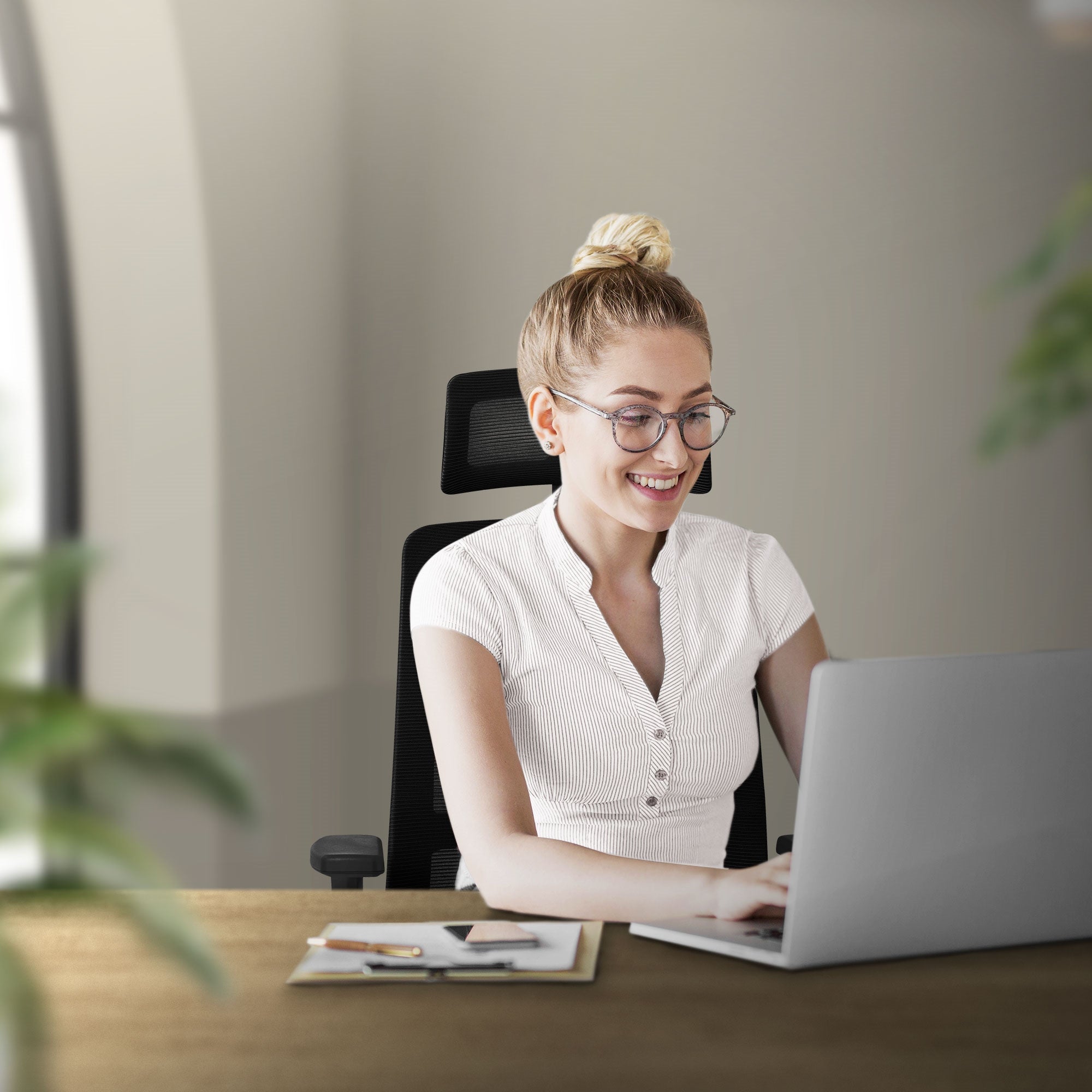 Eine lächelnde Frau sitzt an einem Schreibtisch und arbeitet am Laptop.