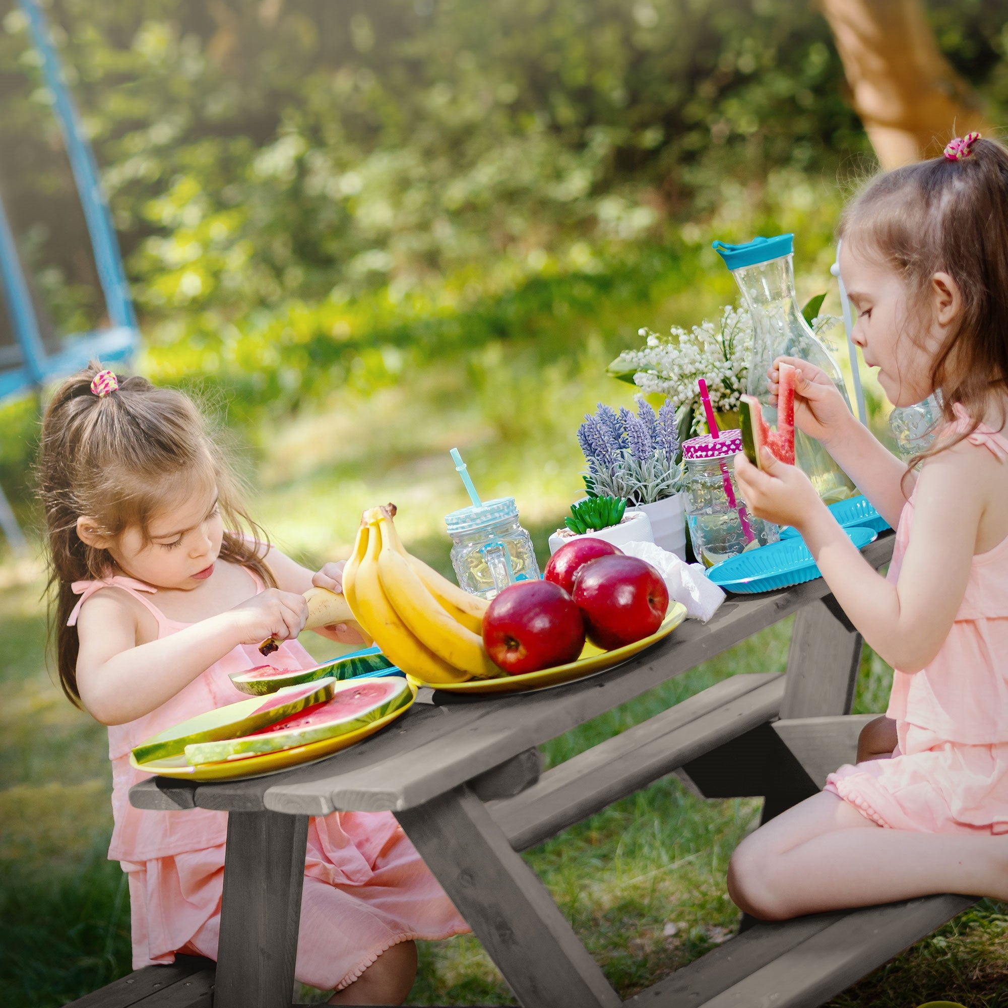 Two girls are playing outside with fruit and dishes on a table.