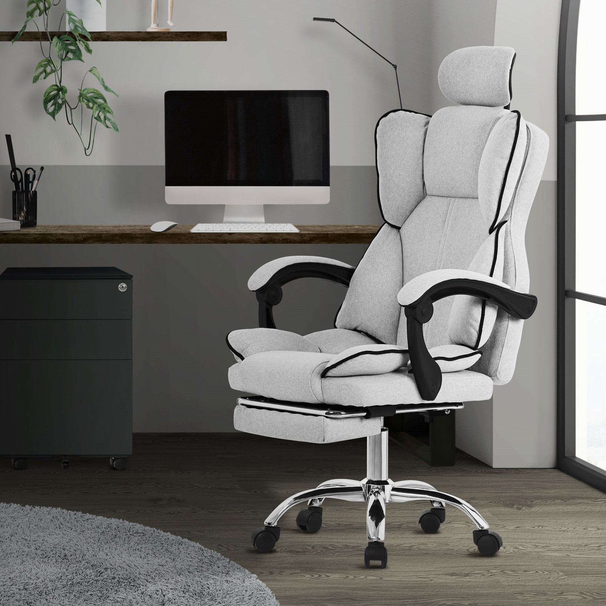 Une chaise de bureau grise avec accoudoirs devant un bureau et un ordinateur.