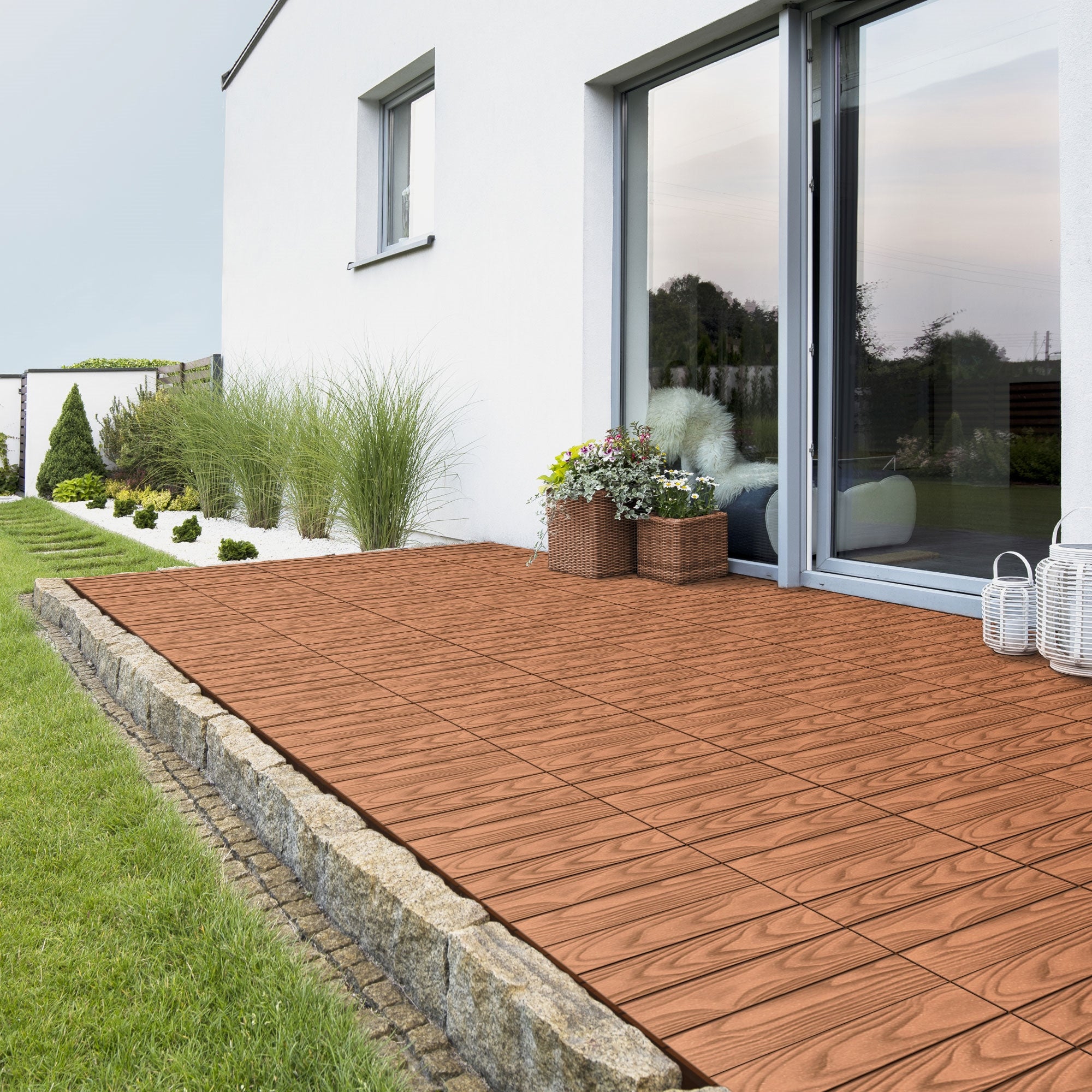 Terras met tegels, planten en een modern huis.