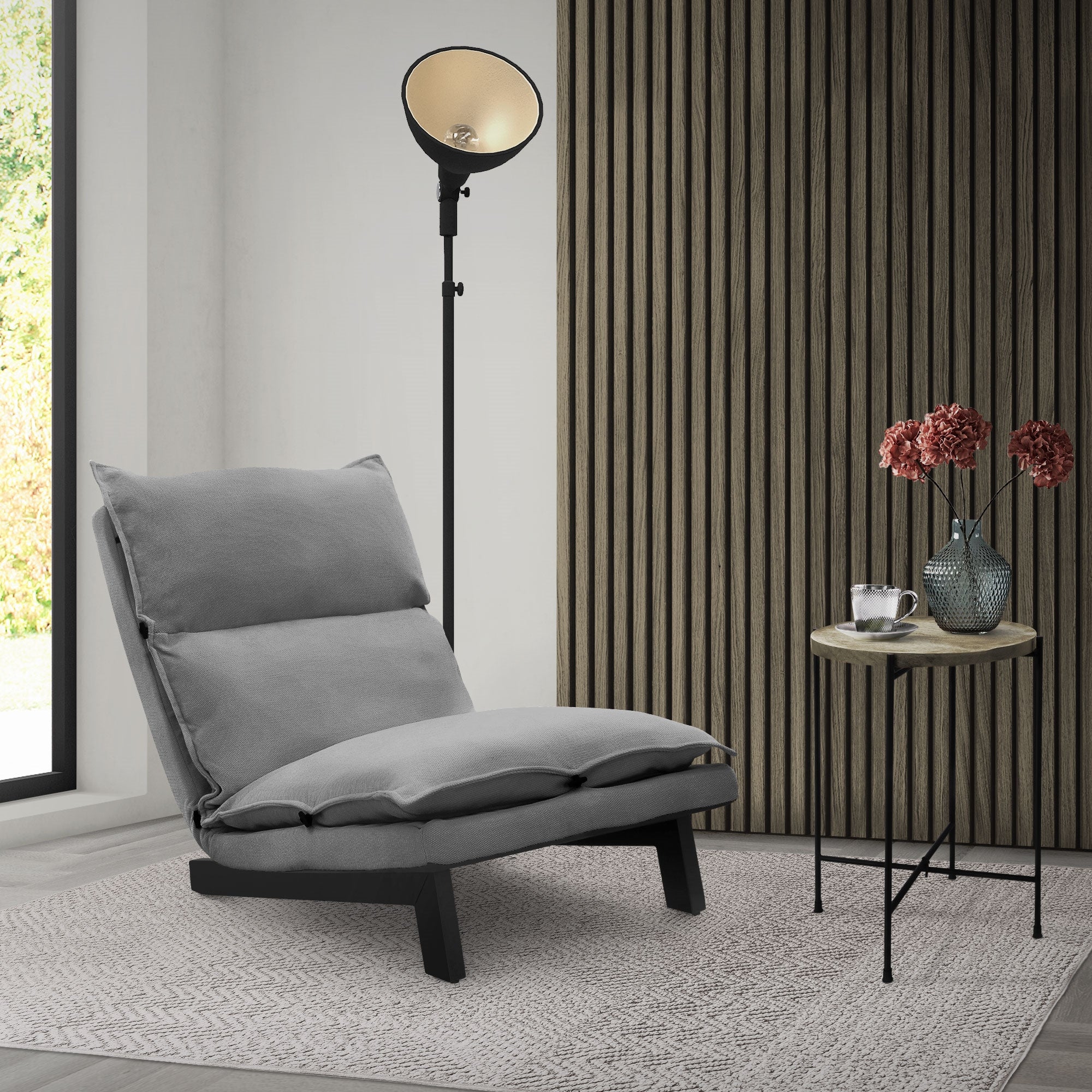 Bequemer grauer Sessel neben einem Tisch mit Blumen und einer Lampe.