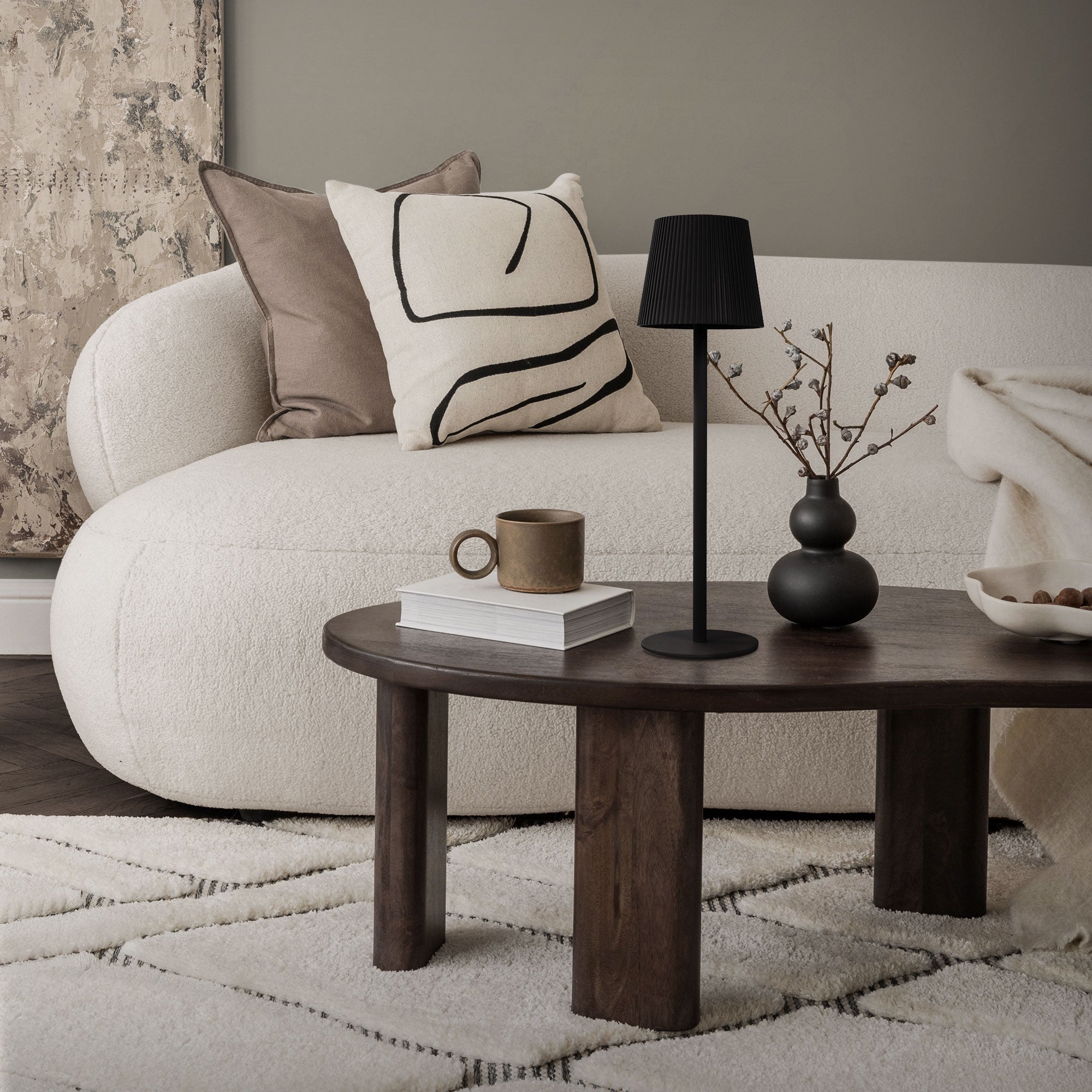 Wohnzimmer mit schwarzer Stehlampe, runder Holztisch und Sofa.