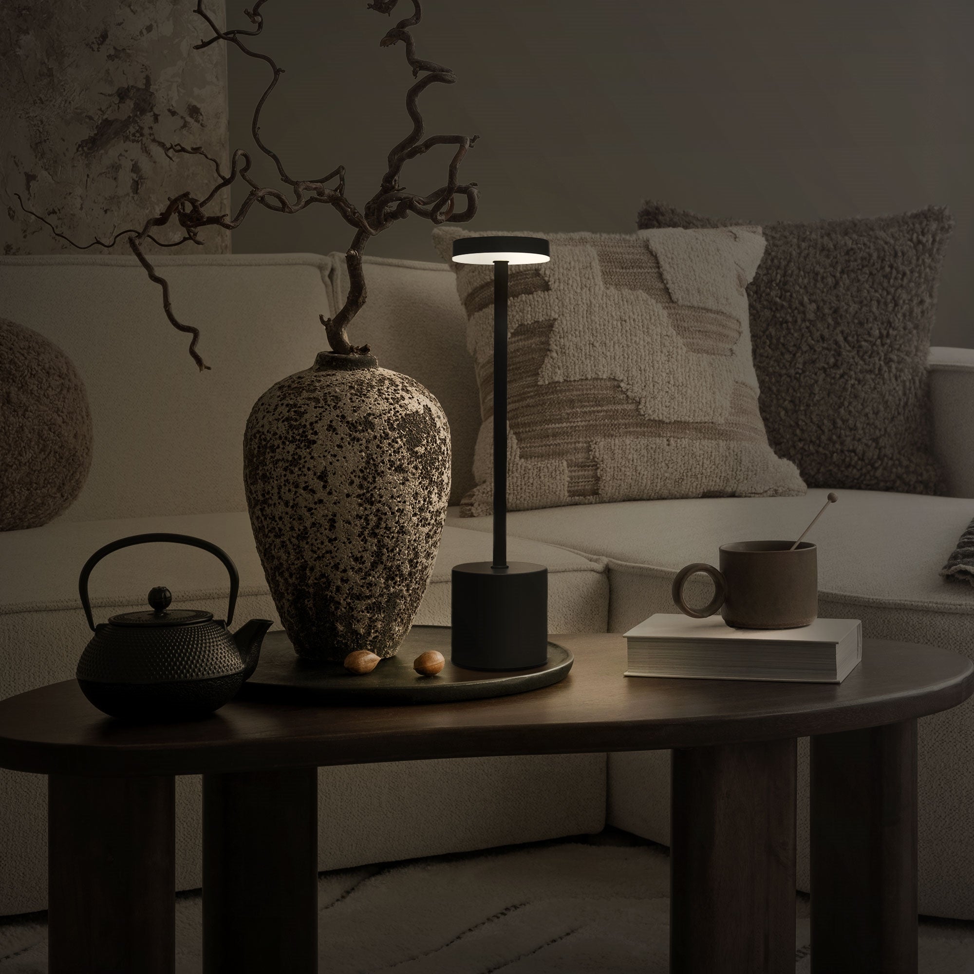 Stehlampe auf einem Tisch neben einer Vase und einer Teekanne.