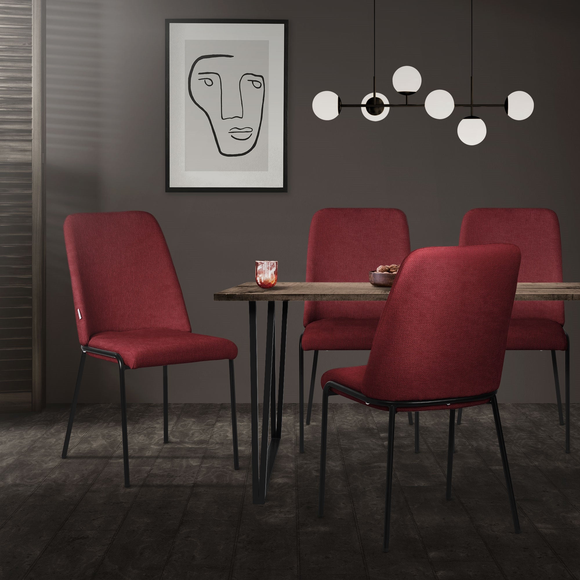 Un área de comedor con una mesa y cuatro sillas rojas, en la pared una imagen abstracta.
