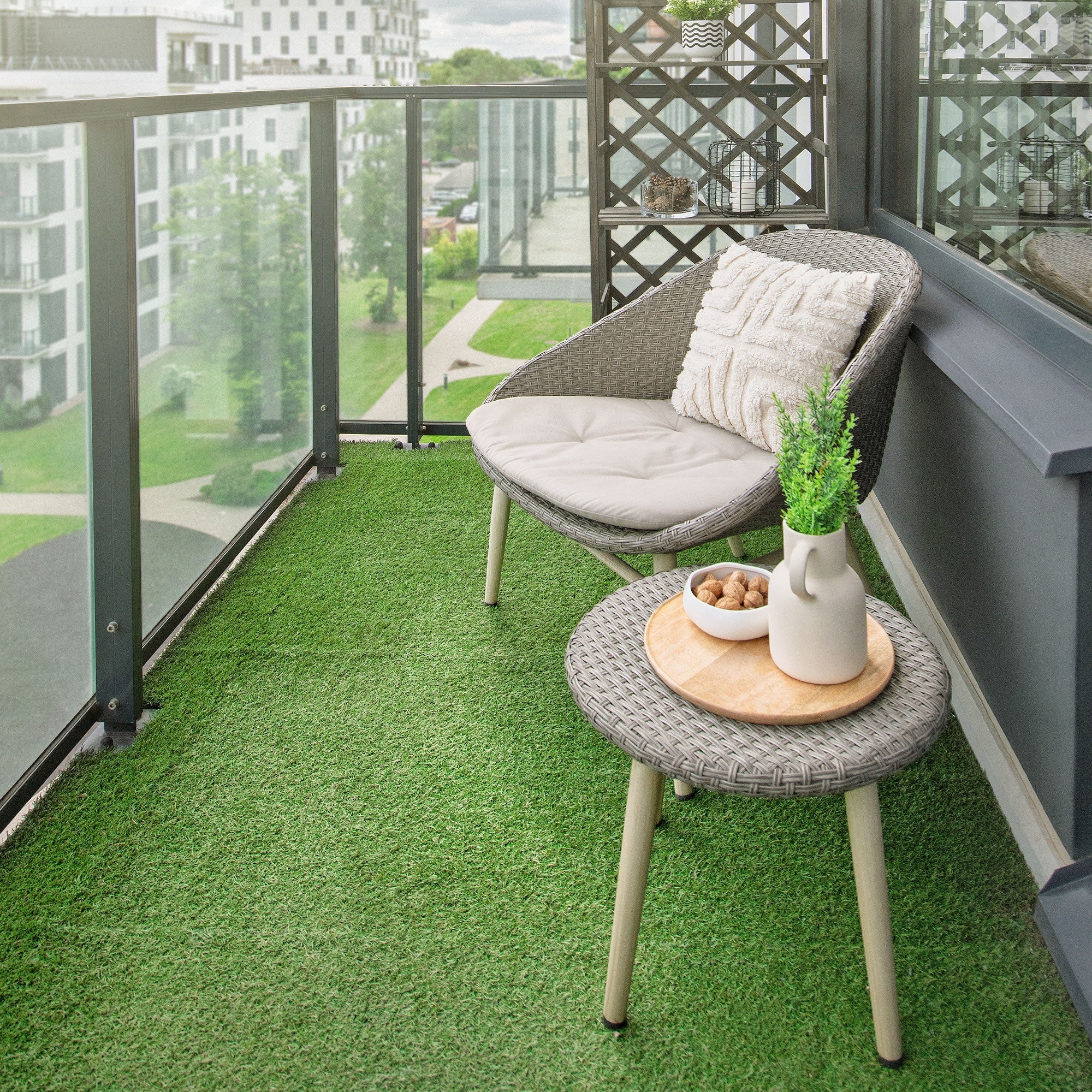 Balkon mit einem grauen Stuhl, einem Tisch und einer Pflanze auf grünem Kunstgras.