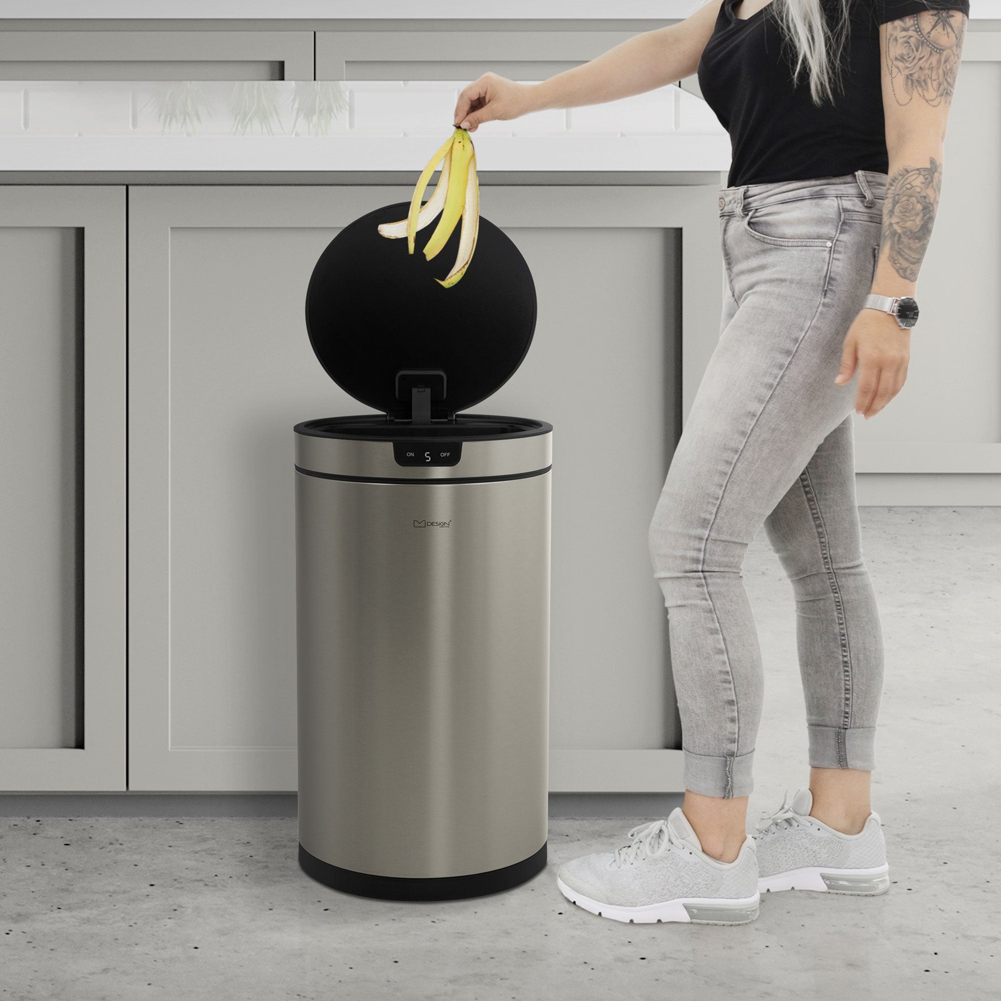 Persona con capelli lunghi che getta banane in un cestino in acciaio inox.