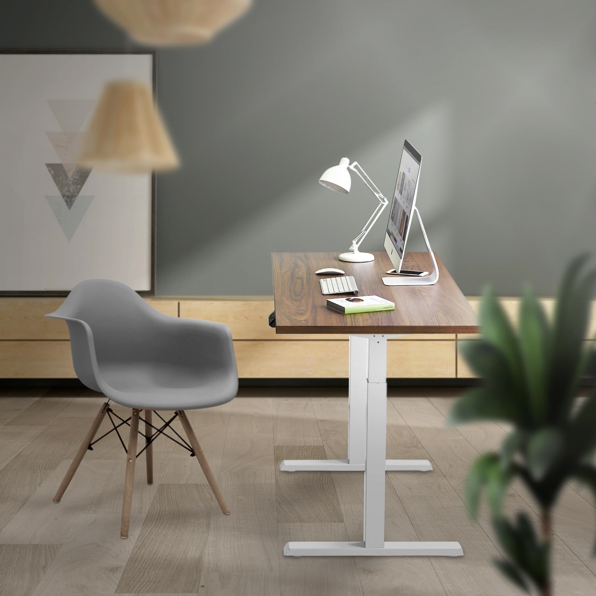 Modern workplace with standing desk, computer, and desk lamp.