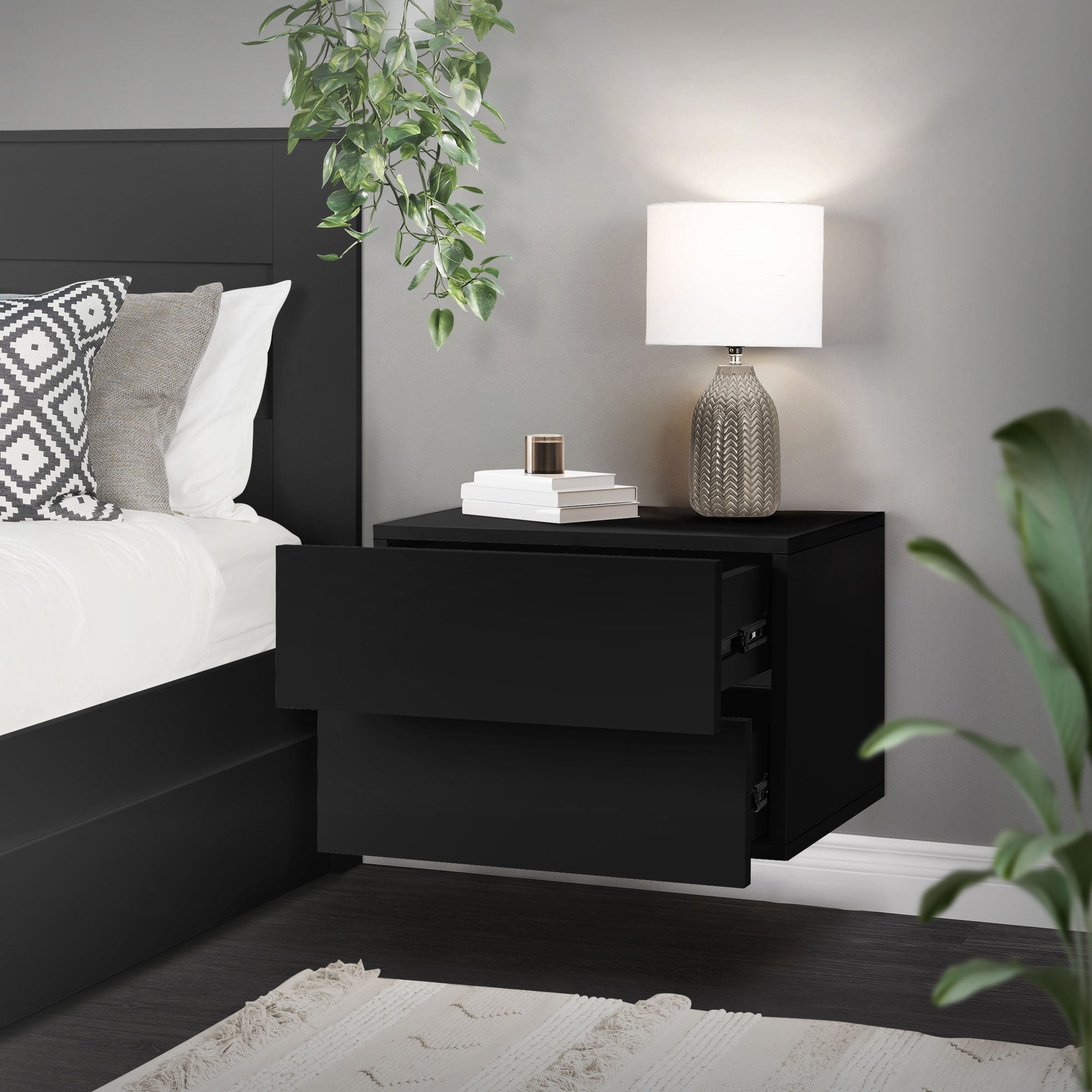 Table de nuit noire avec deux tiroirs ouverts, lampe et plantes en arrière-plan.