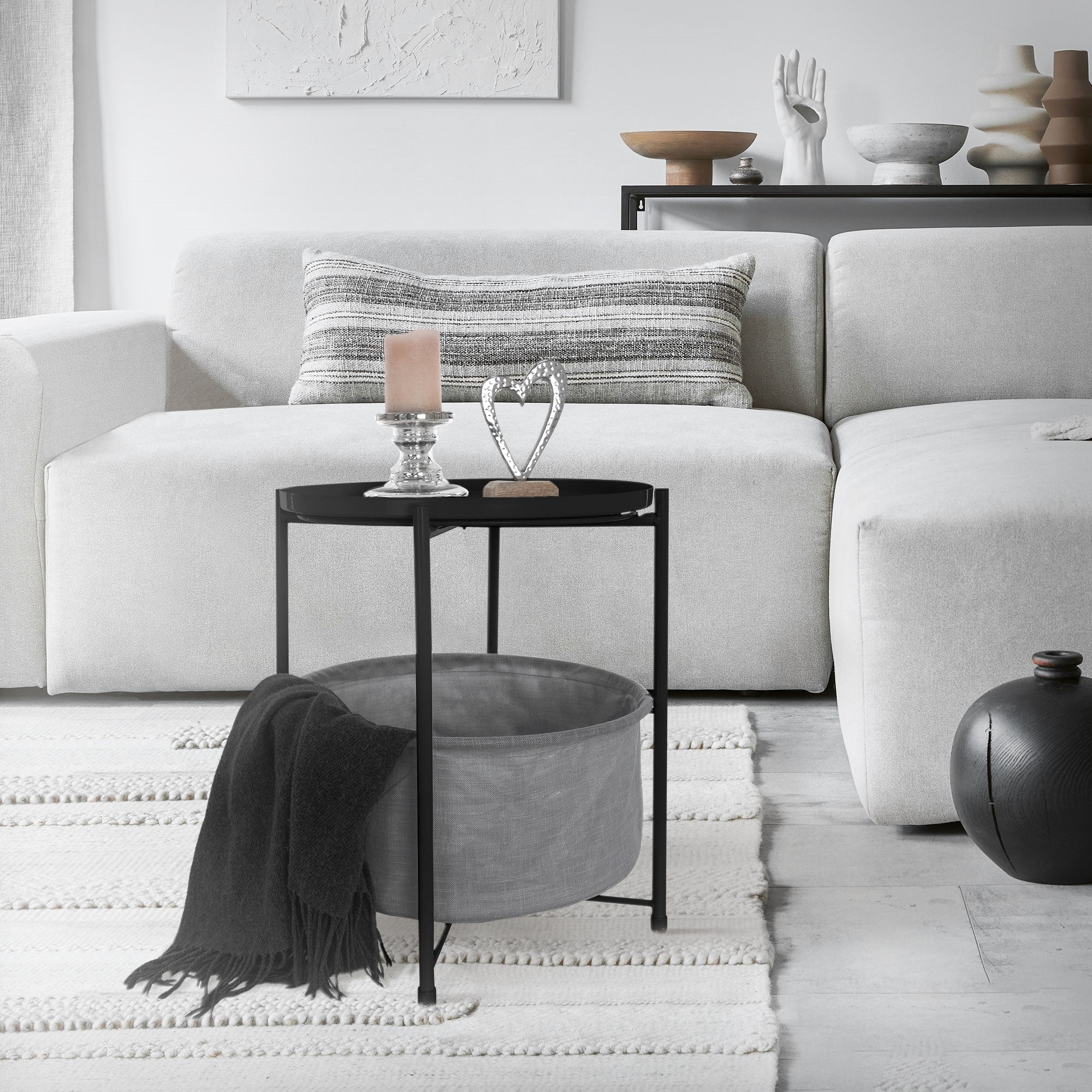 Mesa negra con bolsa gris, sobre un sofá claro y una alfombra en una sala de estar.