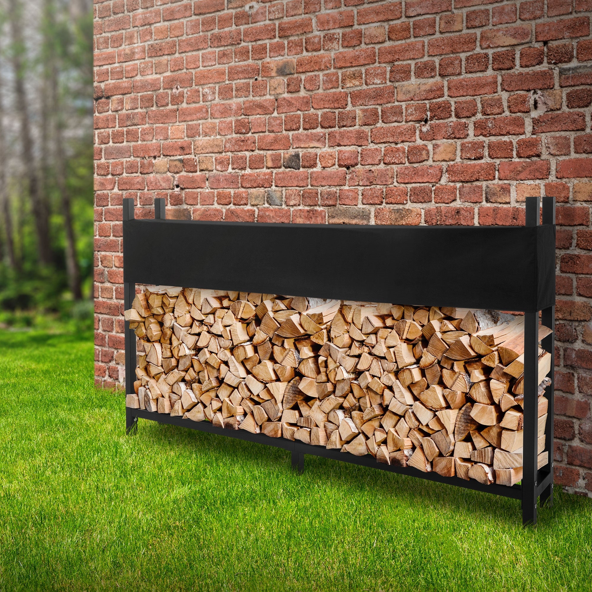 A wood storage made of wood logs in front of a brick wall on green grass.