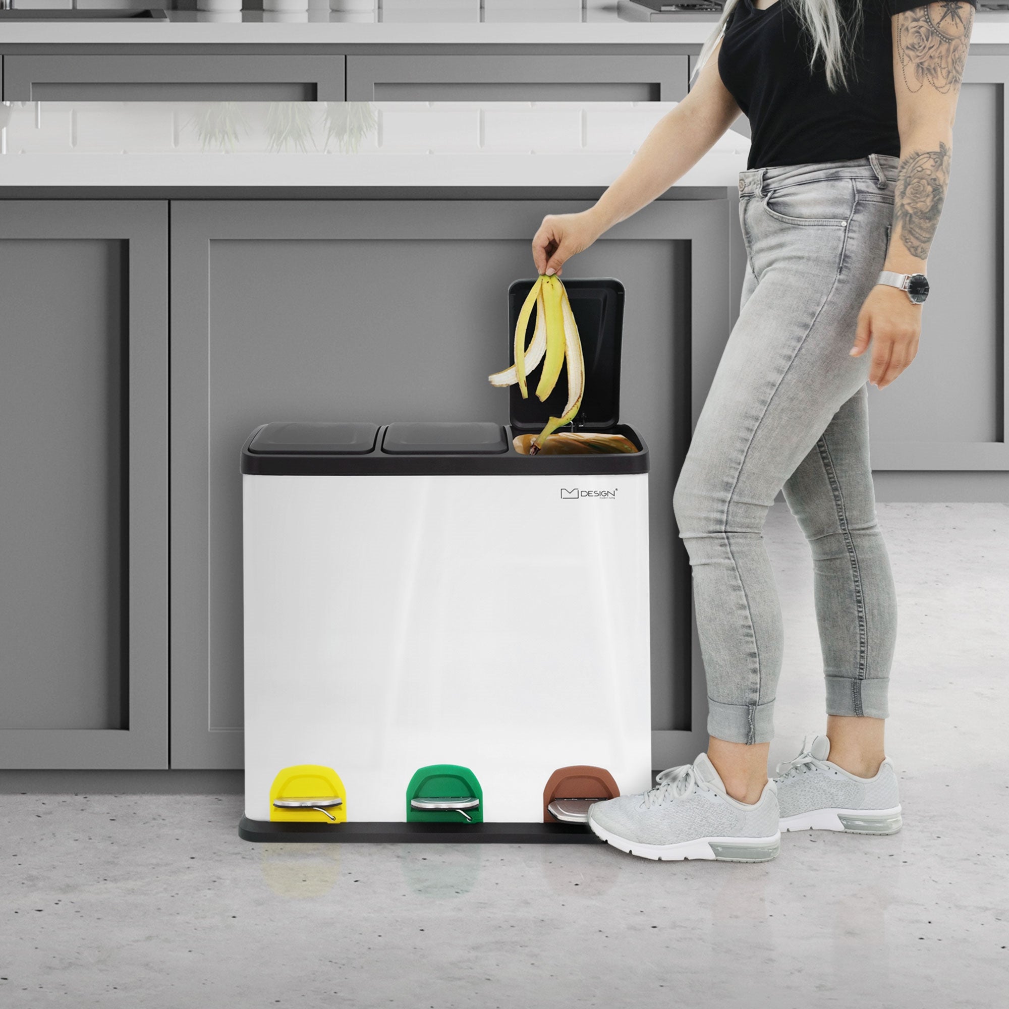 Person mit langen Haaren, die eine Banane in einen Müllimer mit drei Fächern wirft.