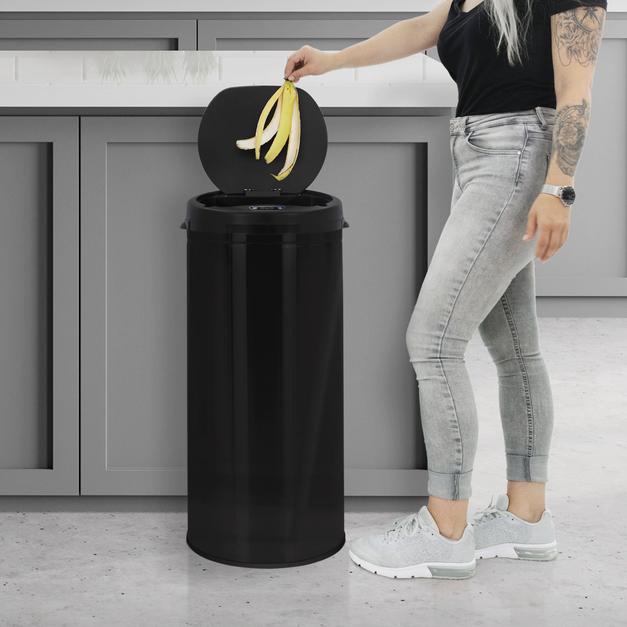 Eine Person wirft eine Banane in einen schwarzen Mülleimer in einer modernen Küche.