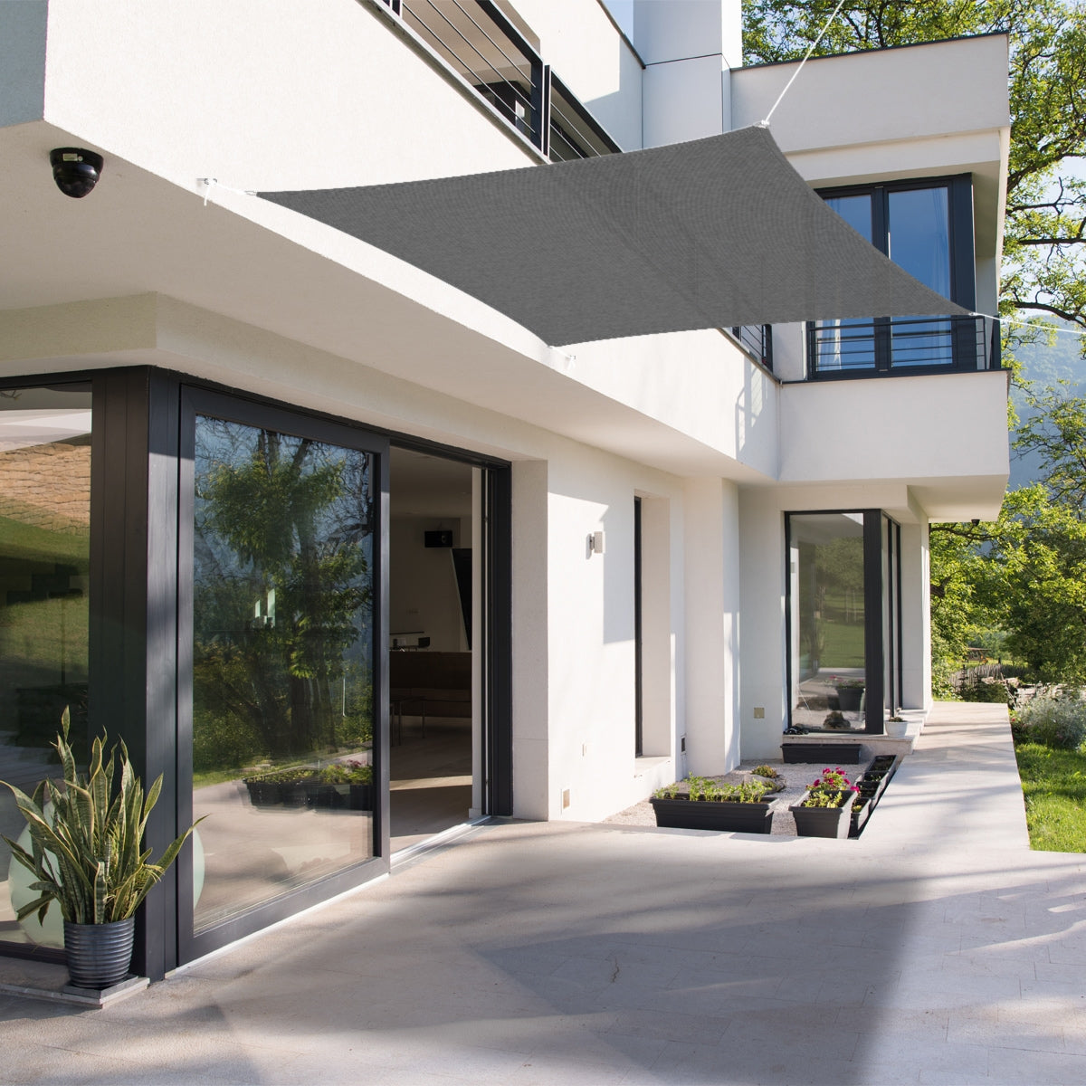 Sonnensegel über einer Terrasse mit Pflanzen und großen Fenstern.