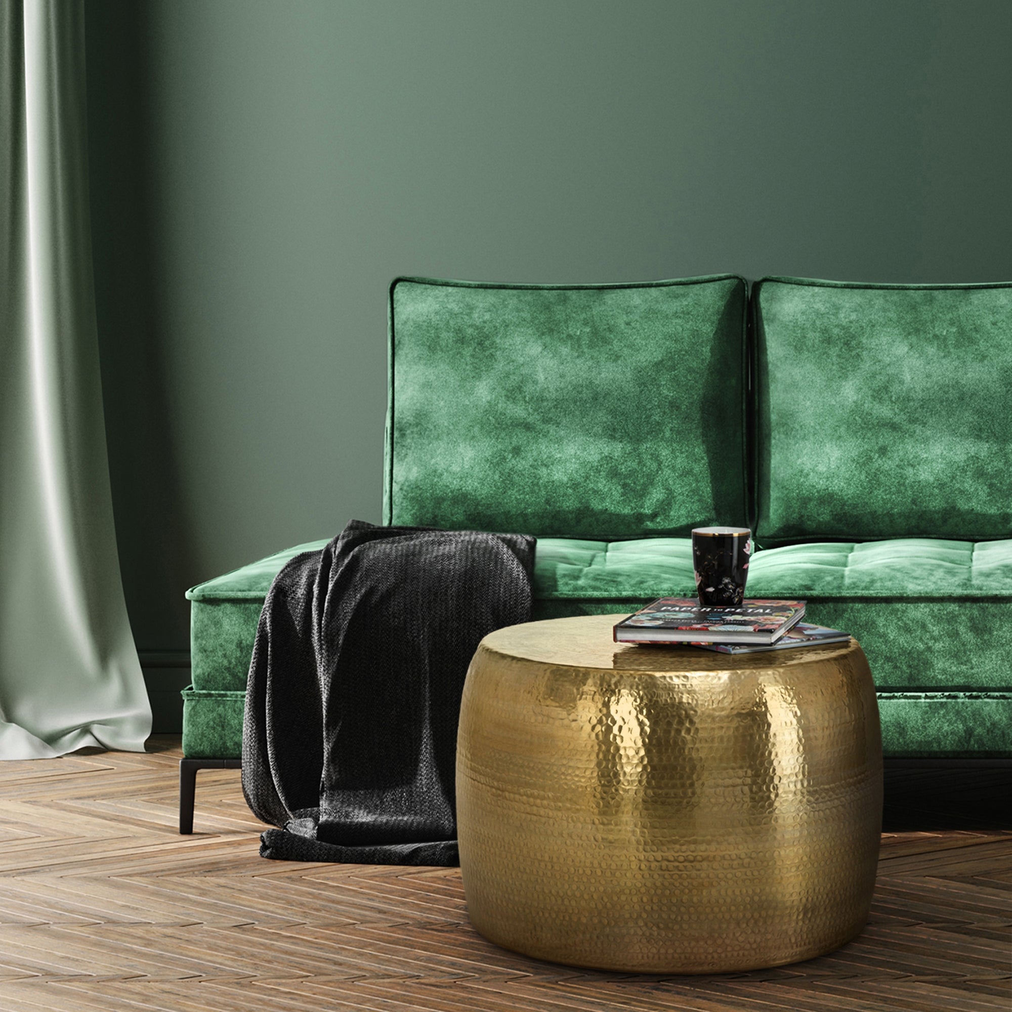 Grünes Sofa mit einer Decke, runder goldfarbener Tisch mit einem Glas und Büchern.