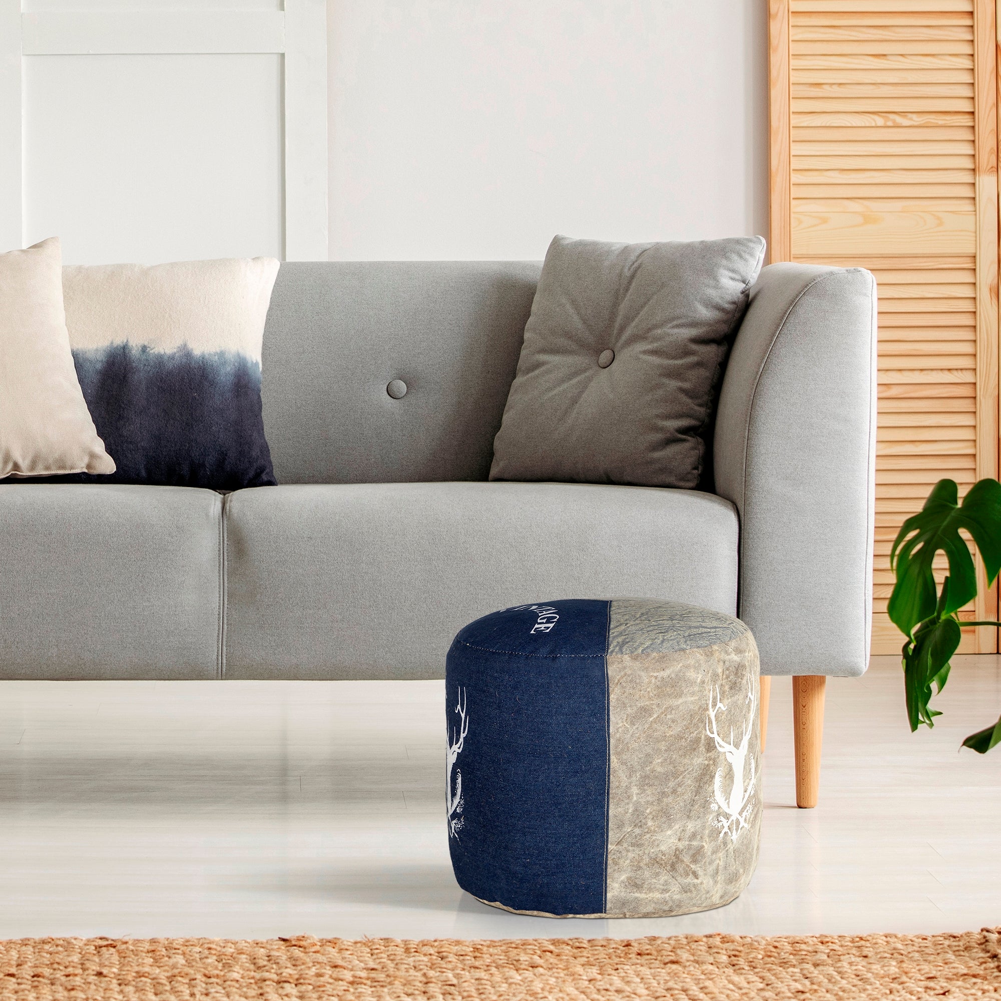 Un pouf rond en tissu denim à côté d'un canapé gris avec des coussins.