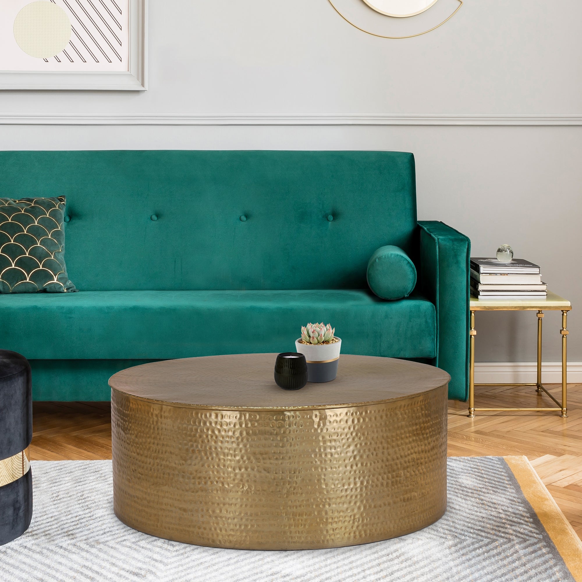 Canapé vert avec des coussins et une table ronde dorée sur un tapis.